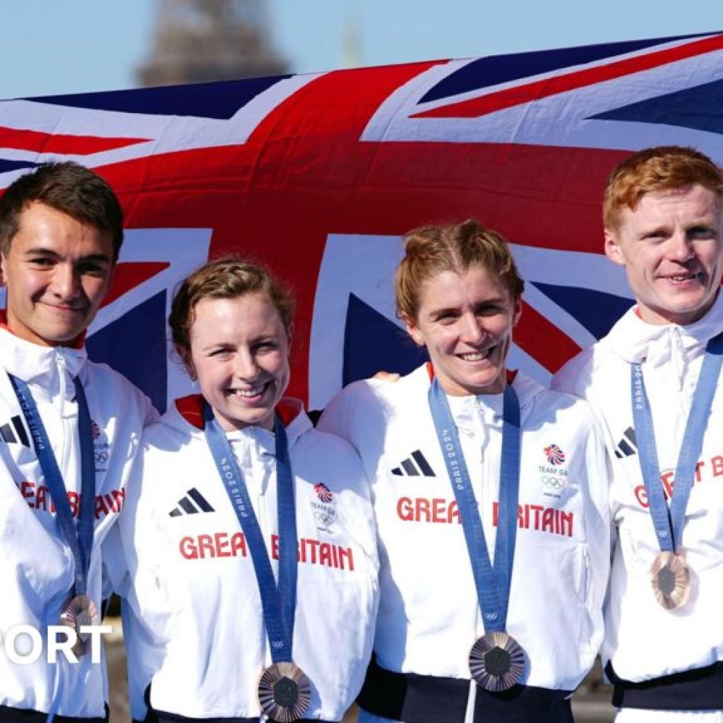 Alex Yee, Georgia Taylor-Brown, Beth Potter and Sam Dickinson pose with a Great Britain flag after winning bronze in the mixed relay triathlon at the Paris 2024 Olympics